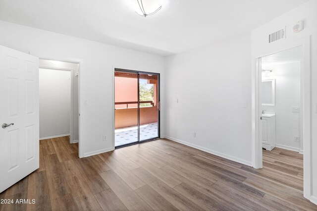 unfurnished bedroom with hardwood / wood-style floors, connected bathroom, and access to exterior