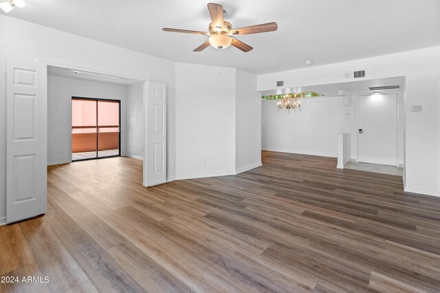 spare room with ceiling fan with notable chandelier and wood-type flooring