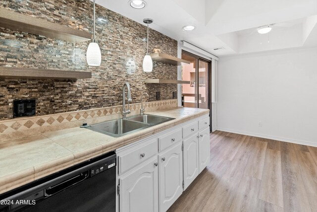 kitchen featuring light wood-type flooring, a raised ceiling, white cabinetry, sink, and black dishwasher