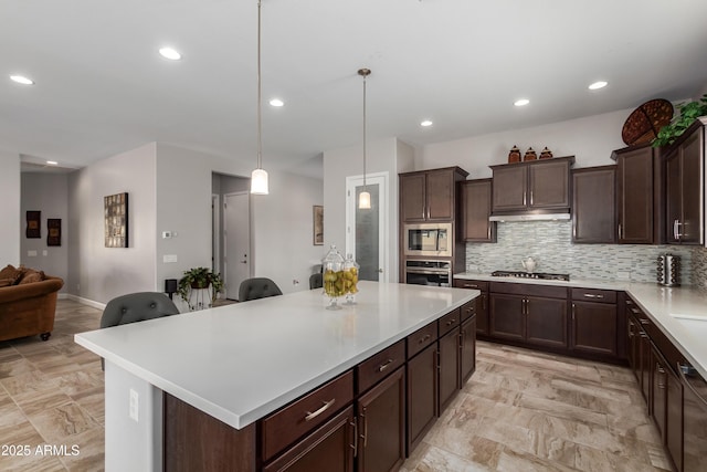 kitchen with a center island, tasteful backsplash, light countertops, appliances with stainless steel finishes, and under cabinet range hood