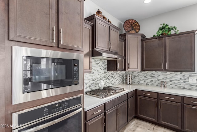 kitchen with dark brown cabinetry, under cabinet range hood, appliances with stainless steel finishes, and decorative backsplash