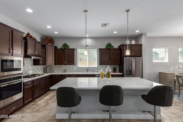 kitchen with visible vents, a center island, stainless steel appliances, light countertops, and under cabinet range hood