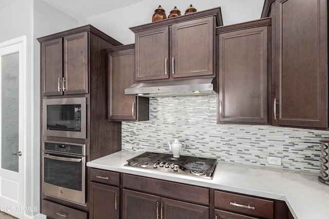 kitchen with stainless steel appliances, light countertops, backsplash, dark brown cabinets, and under cabinet range hood