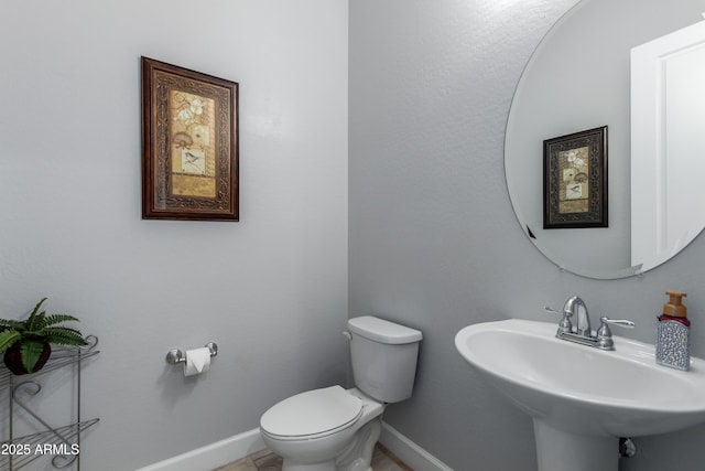 half bathroom with baseboards, a sink, and toilet