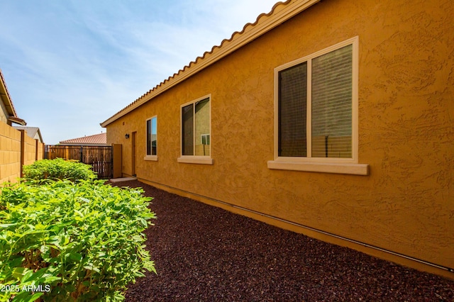 view of side of home with fence, a tile roof, and stucco siding