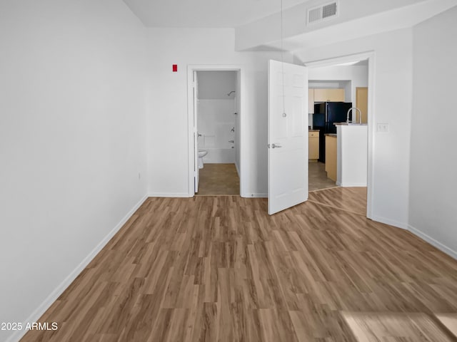 unfurnished bedroom with ensuite bathroom, black refrigerator, and wood-type flooring