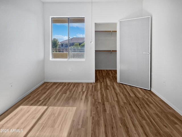 unfurnished bedroom with a spacious closet, a closet, and hardwood / wood-style flooring