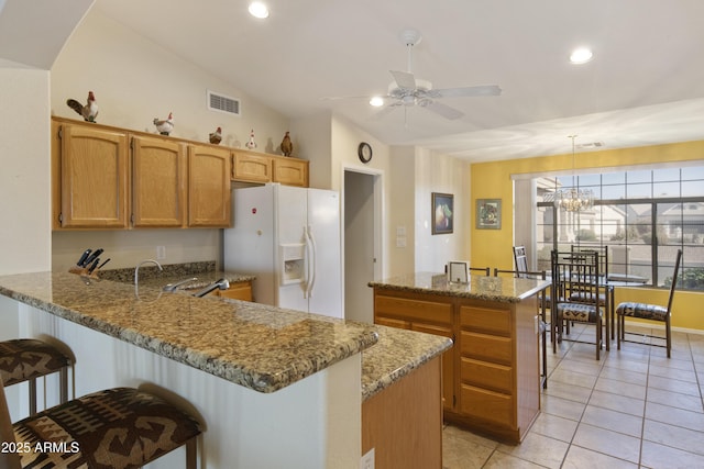 kitchen featuring light stone counters, white refrigerator with ice dispenser, light tile patterned flooring, decorative light fixtures, and kitchen peninsula