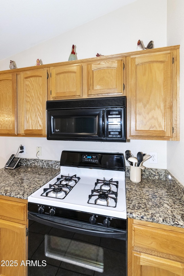 kitchen featuring lofted ceiling, range with gas stovetop, and dark stone countertops