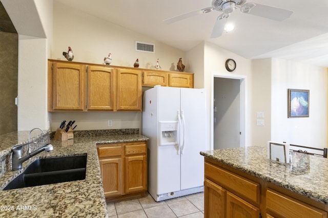 kitchen with lofted ceiling, sink, light tile patterned floors, light stone countertops, and white fridge with ice dispenser