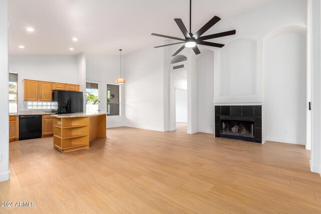 kitchen with pendant lighting, high vaulted ceiling, black appliances, light stone counters, and light hardwood / wood-style floors