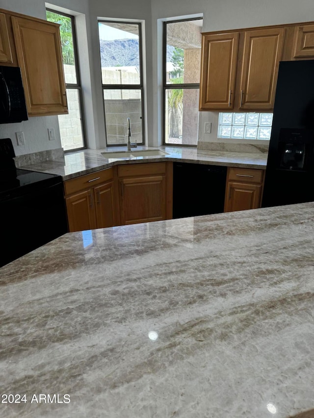 kitchen featuring black appliances, light stone countertops, and sink