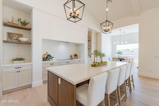 kitchen with light hardwood / wood-style floors, decorative light fixtures, vaulted ceiling with beams, a kitchen island with sink, and a chandelier