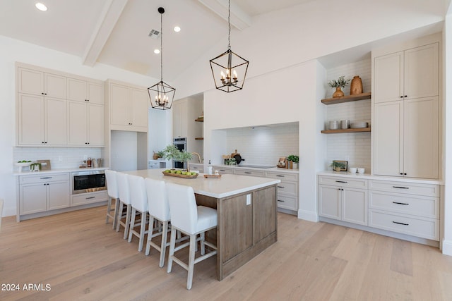 kitchen featuring light hardwood / wood-style floors, tasteful backsplash, beam ceiling, stainless steel microwave, and a center island with sink