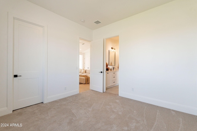 unfurnished bedroom featuring light colored carpet and ensuite bathroom