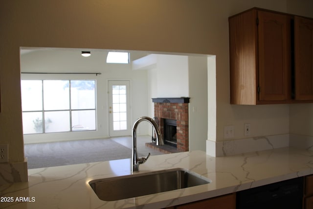 kitchen featuring brown cabinets, black dishwasher, a fireplace, and a sink