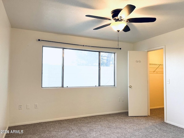 unfurnished bedroom featuring a textured ceiling, a spacious closet, carpet floors, and baseboards