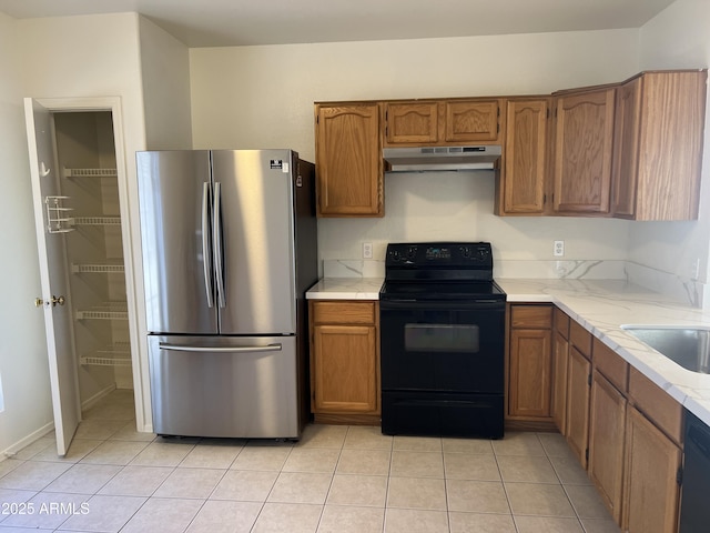 kitchen with brown cabinetry, light countertops, under cabinet range hood, and black appliances