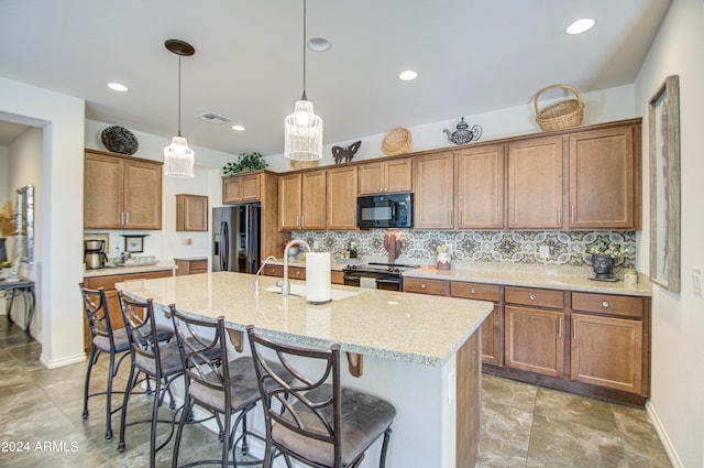 kitchen with light stone counters, pendant lighting, a center island with sink, black appliances, and a breakfast bar