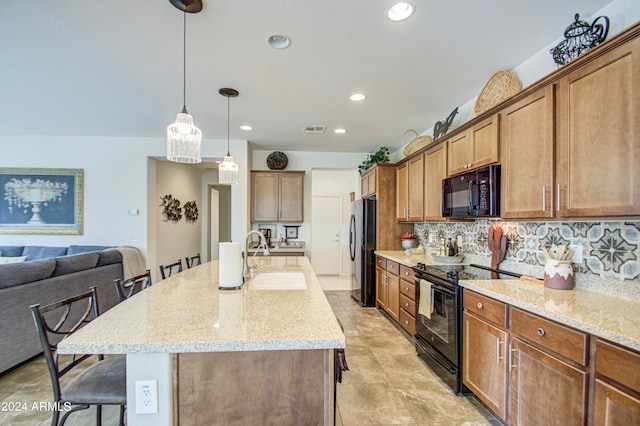 kitchen with a kitchen breakfast bar, an island with sink, pendant lighting, black appliances, and sink