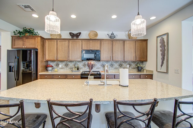 kitchen featuring hanging light fixtures, black appliances, a center island with sink, and an inviting chandelier