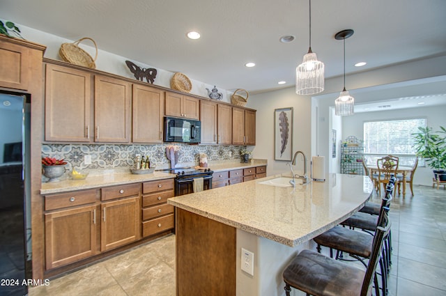 kitchen featuring an island with sink, a kitchen breakfast bar, sink, and black appliances