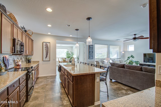 kitchen featuring pendant lighting, black electric range, an island with sink, backsplash, and ceiling fan