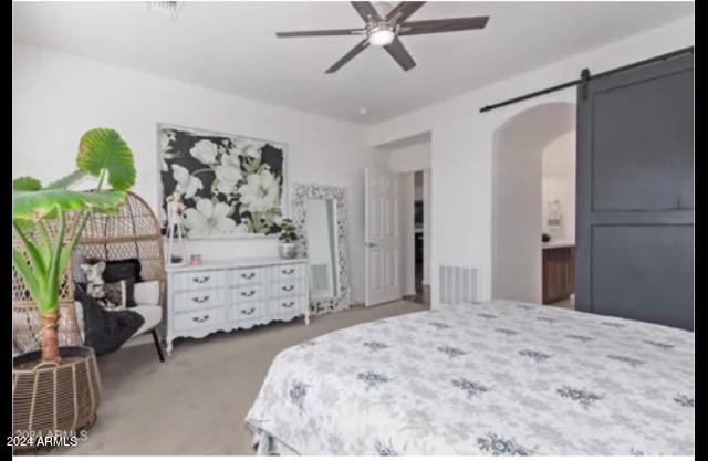 carpeted bedroom with ceiling fan and a barn door