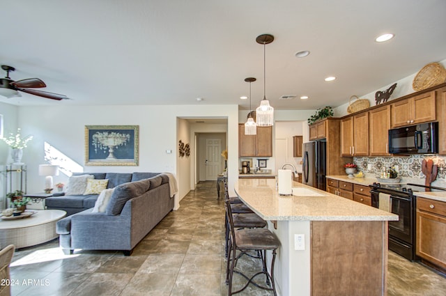 kitchen with pendant lighting, a kitchen island with sink, a breakfast bar area, black appliances, and ceiling fan