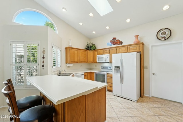 kitchen featuring light countertops, a peninsula, a skylight, white appliances, and a sink