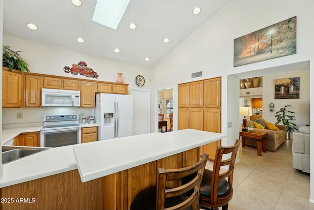 kitchen featuring visible vents, a kitchen bar, white appliances, a skylight, and light tile patterned floors