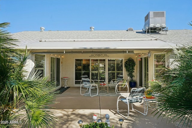 rear view of property featuring central air condition unit, a shingled roof, stucco siding, and a patio area