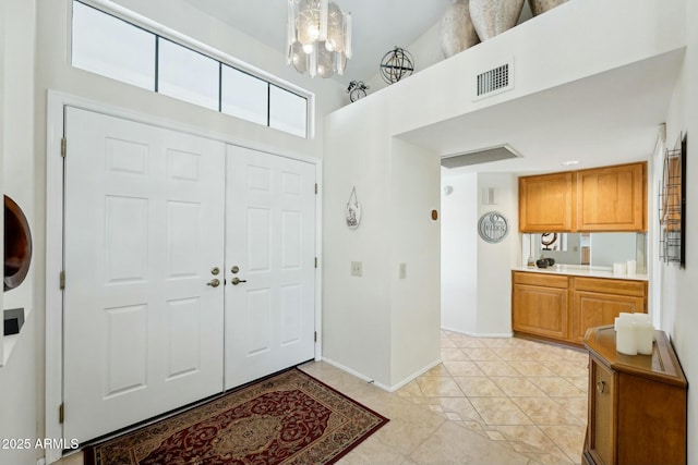 entryway with light tile patterned floors, baseboards, visible vents, a towering ceiling, and a chandelier