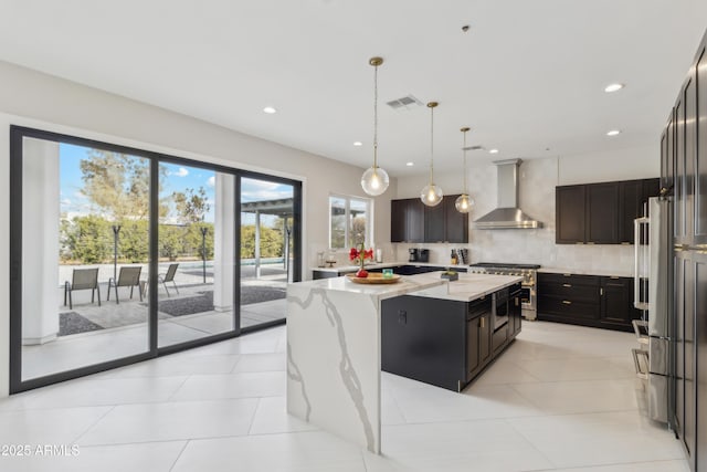 kitchen with backsplash, hanging light fixtures, a spacious island, light stone countertops, and wall chimney exhaust hood