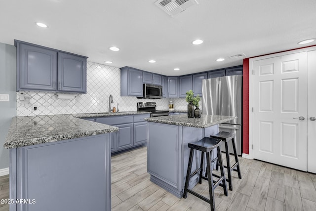 4116 E Downing St, Mesa, AZ 85205 - kitchen featuring appliances with stainless steel finishes, stone countertops, light wood finished floors, a kitchen breakfast bar, and tasteful backsplash