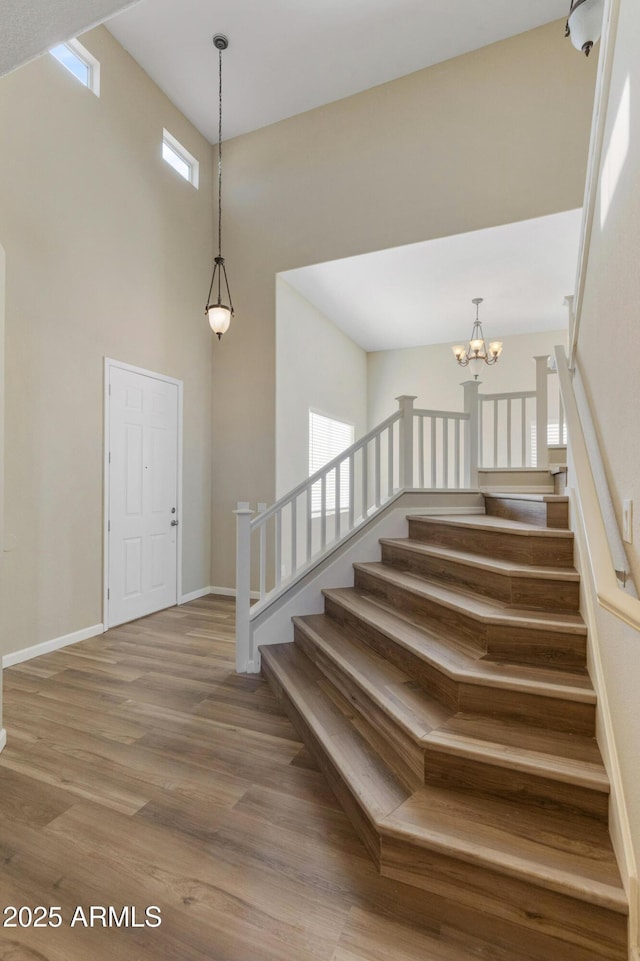 stairs featuring a chandelier, a towering ceiling, and wood-type flooring