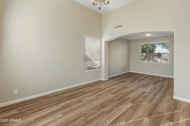 spare room with a towering ceiling, an inviting chandelier, and hardwood / wood-style floors