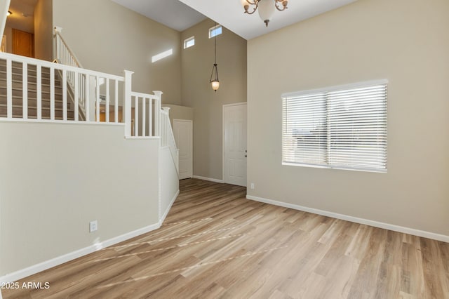 empty room featuring an inviting chandelier, a wealth of natural light, light hardwood / wood-style floors, and a towering ceiling