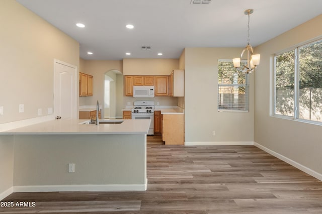 kitchen with an inviting chandelier, kitchen peninsula, white appliances, light brown cabinetry, and hanging light fixtures