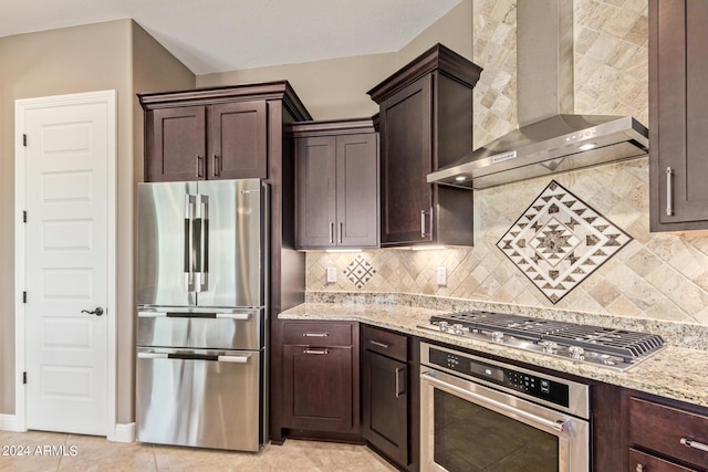 kitchen with tasteful backsplash, light stone counters, stainless steel appliances, wall chimney range hood, and light tile patterned floors