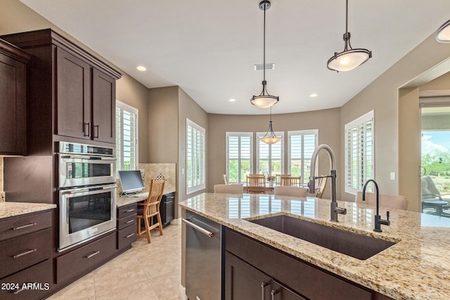 kitchen featuring appliances with stainless steel finishes, light stone counters, pendant lighting, and sink