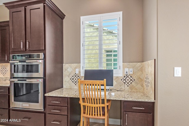 kitchen featuring light stone countertops, built in desk, backsplash, and double oven