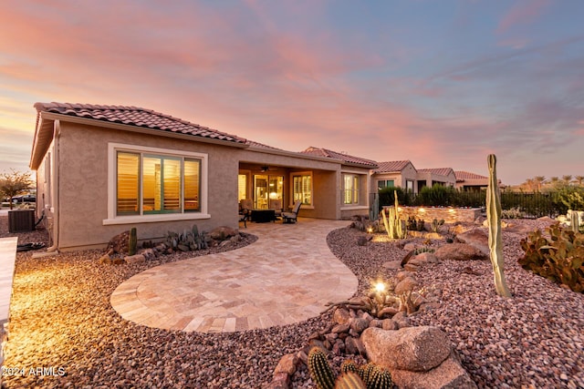 back house at dusk with central AC unit and a patio area