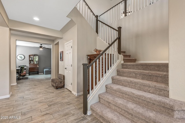 stairway with ceiling fan, recessed lighting, wood finish floors, a towering ceiling, and baseboards