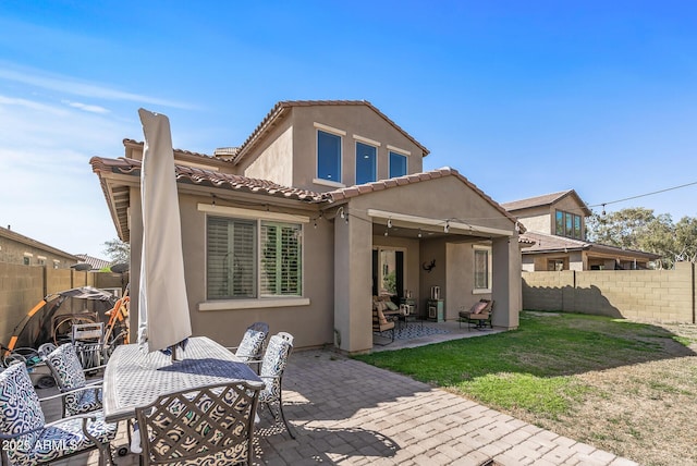 rear view of property with fence, a yard, a tiled roof, stucco siding, and a patio area