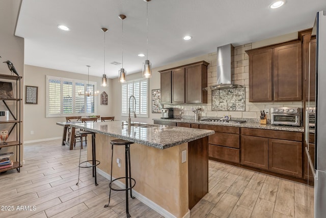 kitchen with decorative backsplash, stone countertops, wood tiled floor, a sink, and wall chimney range hood