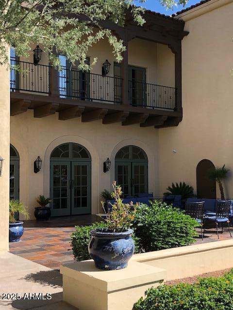 view of exterior entry featuring french doors, a patio area, a balcony, and stucco siding