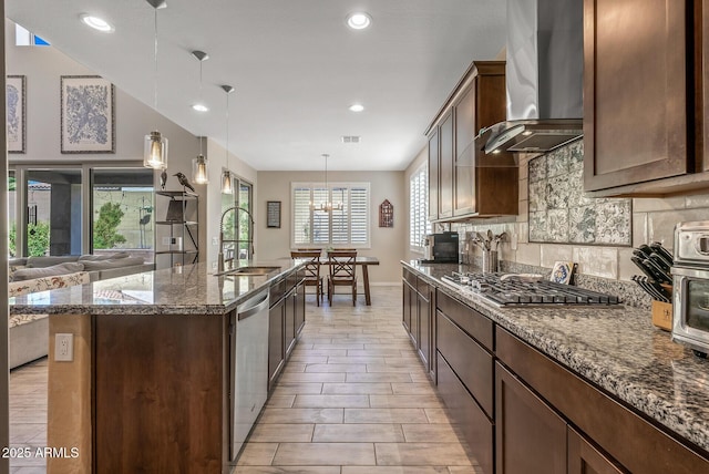 kitchen featuring a center island with sink, tasteful backsplash, appliances with stainless steel finishes, a sink, and wall chimney exhaust hood