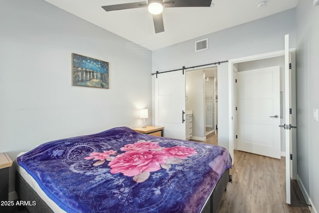 bedroom featuring hardwood / wood-style flooring, ensuite bath, a barn door, and ceiling fan