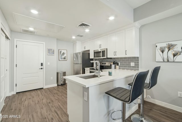 kitchen with a kitchen bar, kitchen peninsula, white cabinets, stainless steel appliances, and backsplash